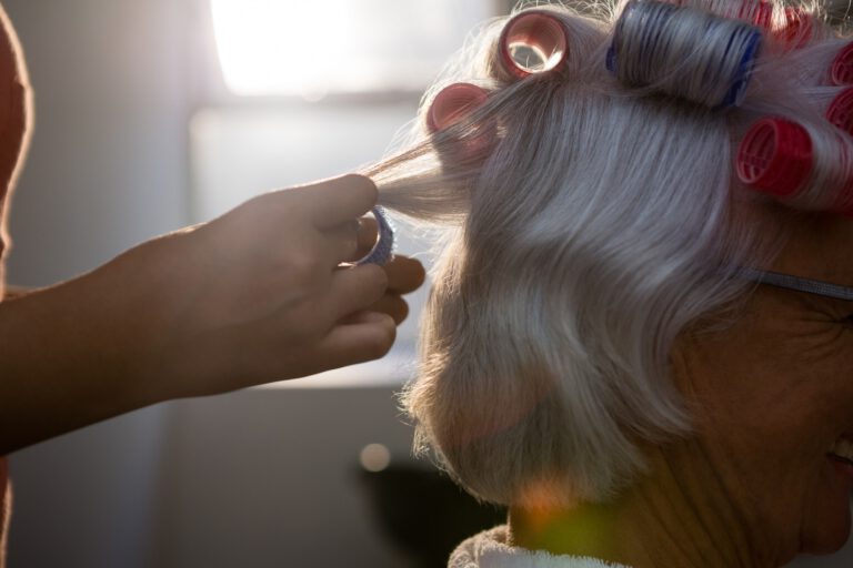 Hands of hairstylist removing curlers from senior woman hair
